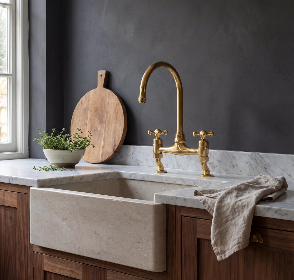 Unlacquered brass bridge kitchen faucet with cross handles on a farmhouse sink