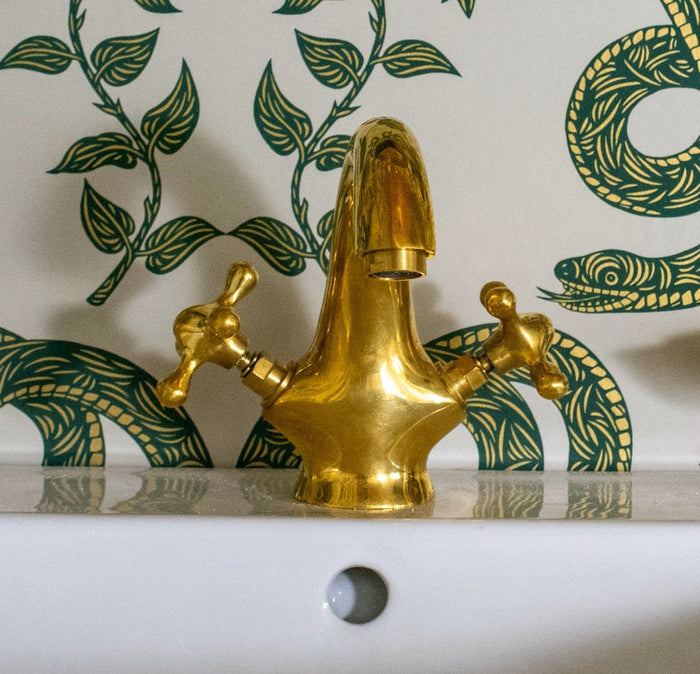 Cross-handle single-hole unlacquered brass vanity faucet — solid brass construction visible in the weight and finish of the handles